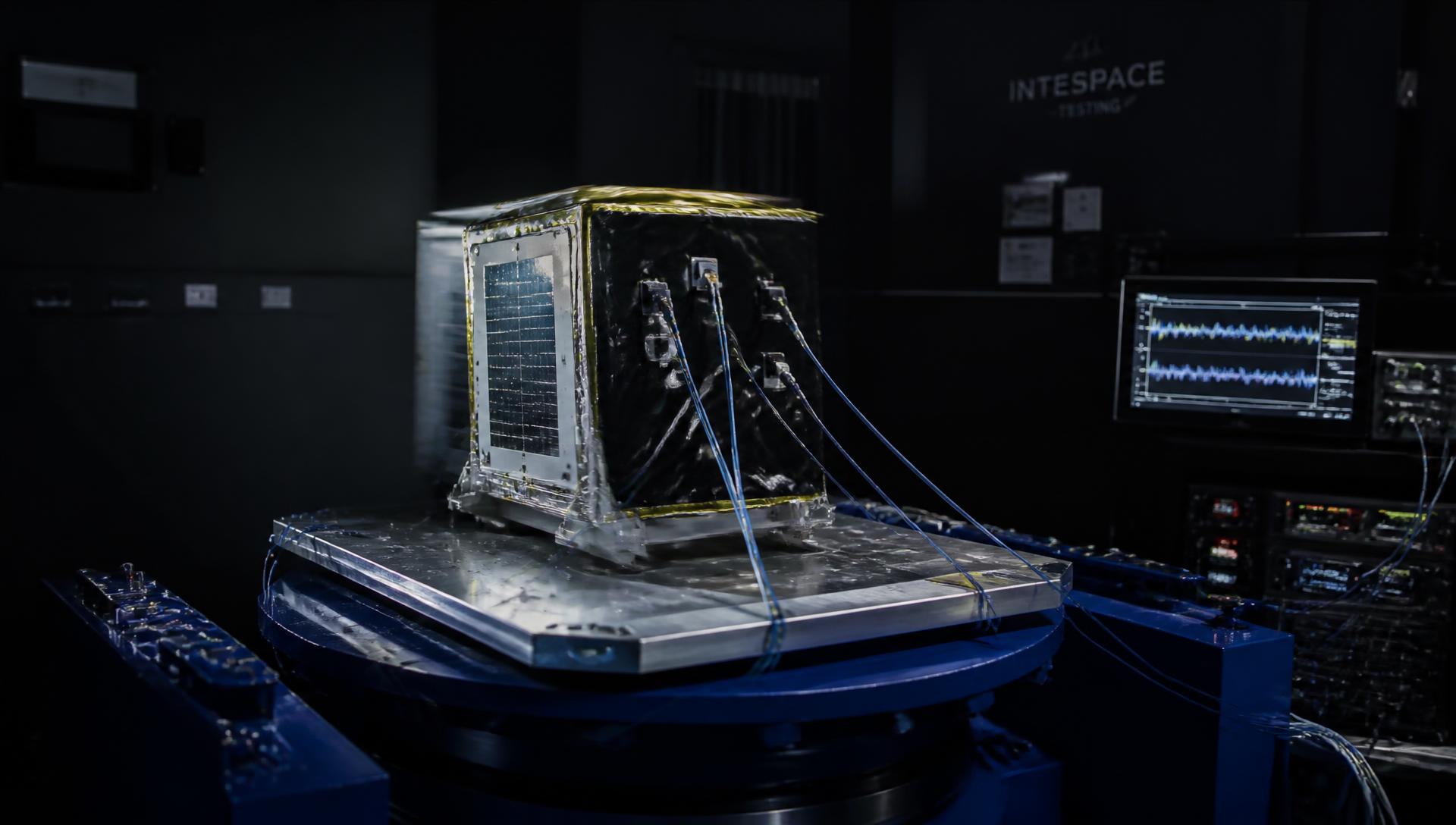 Satellite payload mounted on an electrodynamic vibration shaker table with accelerometer cabling and monitoring screens